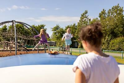 Kinder springen auf dem Lufttrampolin auf dem Spielplatz im Roompot Ferienpark Callassande