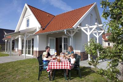 Die Familie isst an einem Tisch im Garten eines Ferienhauses in der Roompot Résidence Klein Vink