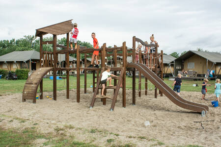 Kinder spielen auf einem Spielplatz auf einem Feld mit Safarizelten im Ferienpark De Boshoek