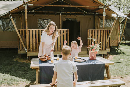 Familie an einem Picknicktisch eines Lodge-Zeltes im Ferienpark Dierenbos