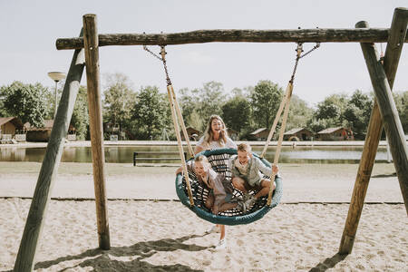 Kinder auf einer großen Schaukel auf einem Spielplatz im Ferienpark Dierenbos