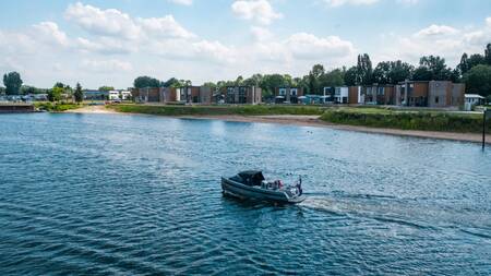Eine Schaluppe segelt vor Ferienhäusern auf dem Wasser im Ferienpark EuroParcs Aan de Maas