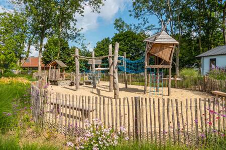 Ein eingezäunter Spielplatz mit Holzspielgeräten im Ferienpark EuroParcs Aan de Maas