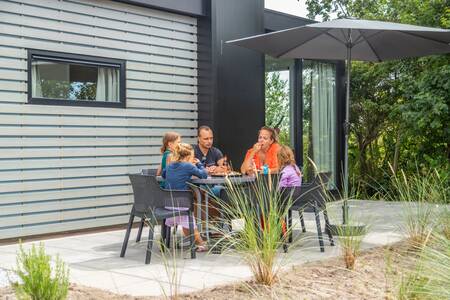 Gezin aan tafel in de tuin van een chalet op vakantiepark EuroParcs De Koog