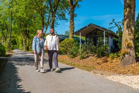 Ein Paar geht vor einem Ferienhaus im Ferienpark EuroParcs De Wije Werelt spazieren