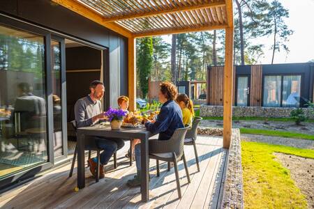 Die Familie isst auf der Veranda eines Chalets im Ferienpark EuroParcs Hoge Kempen