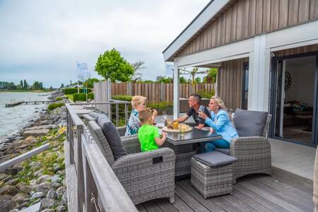 Die Familie isst auf der Veranda eines Chalets am Wasser im Ferienpark EuroParcs Markermeer