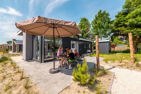 Die Familie sitzt an einem Tisch im Garten eines Ferienhauses im EuroParcs Poort van Zeeland