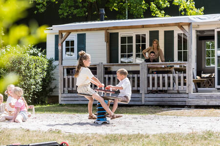 Kinder spielen vor einem Chalet mit überdachter Veranda im Ferienpark Kampeerdorp de Zandstuve