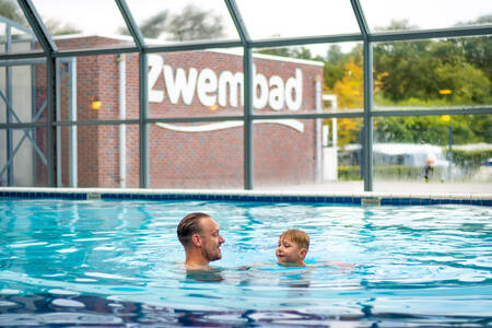 Vater mit Kind schwimmt im Hallenbad von Krieghuusbelten