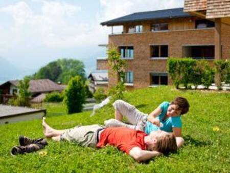 2 Personen liegen auf der Wiese vor einem Apartmentkomplex im Landal Alpen Chalet Matin
