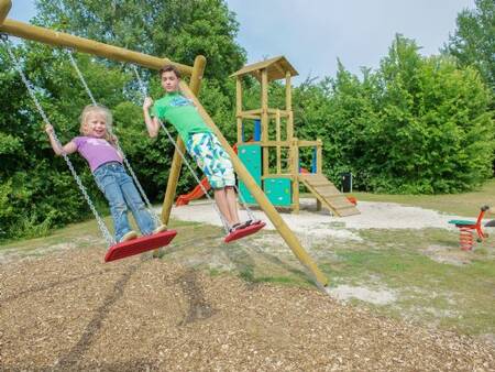 Kinder spielen auf der Schaukel auf einem Spielplatz im Ferienpark Landal De Bloemert