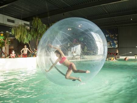 Mädchen in einem großen Ball im Swimmingpool des Ferienparks Landal Esonstad