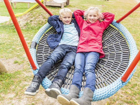 2 Kinder auf einer Schaukel auf einem Spielplatz im Ferienpark Landal Hochwald