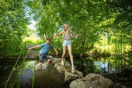 Auf dem Naturspielplatz von Landal Klein Oisterwijk spielen Kinder auf Steinen im Wasser