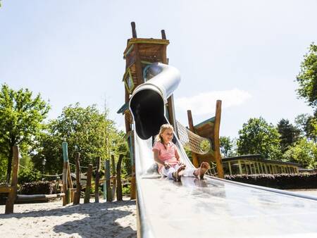 Kind rutscht auf einem Spielplatz im Ferienpark Landal Twenhaarsveld die Rutsche hinunter