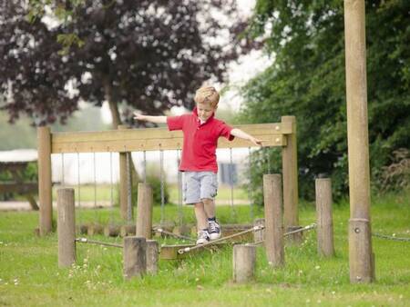 Junge balanciert auf einem Spielgerät auf einem Spielplatz im Landal Waterpark Sneekermeer