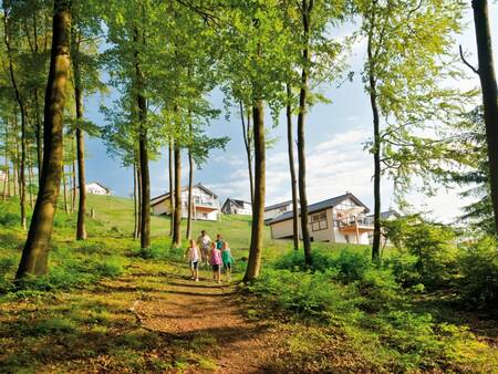 Familienspaziergang zwischen Bäumen mit Ferienhäusern von Landal Winterberg im Hintergrund