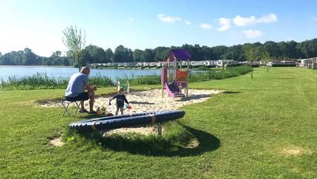 Vater mit Kind auf einem kleinen Spielplatz im Ferienpark Molecaten Park De Agnietenberg