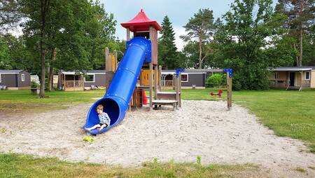 Kind auf der Rutsche auf einem Spielplatz zwischen Chalets im Ferienpark Molecaten Park De Koerberg