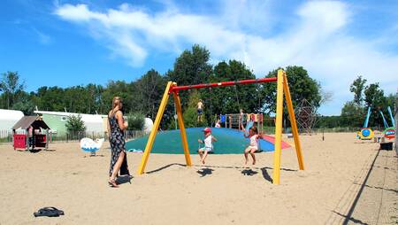 Kinder auf einer Schaukel auf einem Spielplatz im Ferienpark Molecaten Park Rondeweibos