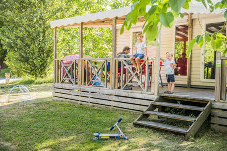 Familie sitzt auf der überdachten Veranda eines Mobilheims im Ferienpark RCN Le Moulin de la Pique
