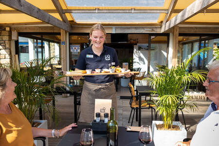 Kellner liefert Snacks an ein Paar auf der Terrasse des Restaurants im Ferienpark RCN Port l'Epine