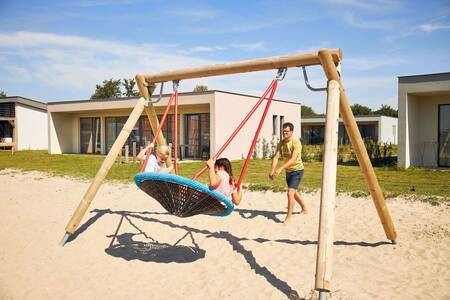 Kinder auf einer Schaukel auf einem Spielplatz im Ferienpark RCN de Schotsman