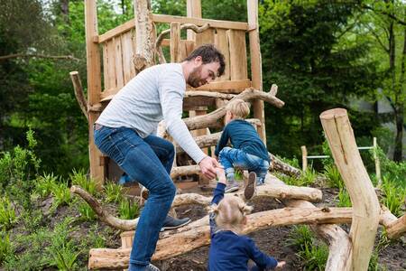 Vater mit Kindern auf einem Holzspielplatz im Ferienpark Roompot Bungalowpark Hoenderloo