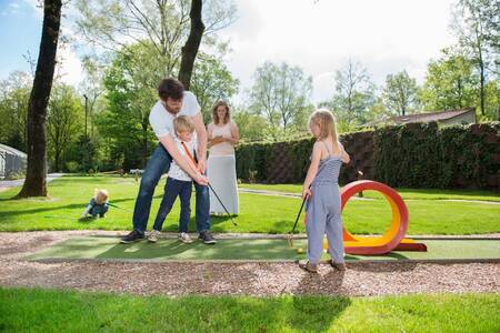 Familie spielt Golf auf der Minigolfanlage des Ferienparks Roompot Bungalowpark Hoenderloo