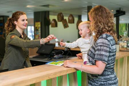 Frau mit Kind erhält Schlüssel an der Rezeption des Roompot Bungalowpark Hoenderloo