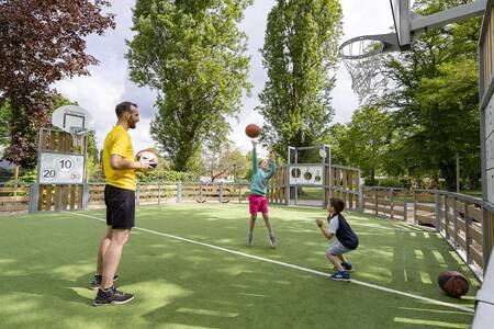 Vater mit 2 Kindern, die auf dem multifunktionalen Sportplatz von Roompot Château des Marais spielen