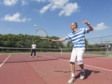 2 Personen spielen Tennis auf dem Tennisplatz des Ferienparks Roompot De Veluwse Hoevegaerde