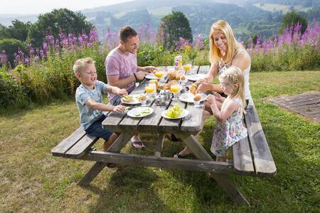 Menschen an einem Picknicktisch im Garten eines Ferienhauses im Roompot Eifelpark Kronenburger See