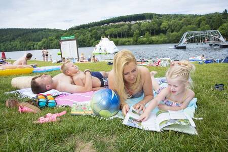 Menschen liegen auf der Wiese am Stausee neben dem Roompot Eifelpark Kronenburger See