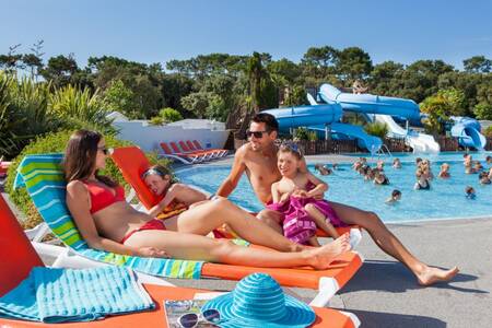 Familie auf Liegestühlen neben dem Außenpool des Ferienparks Roompot Le Littoral