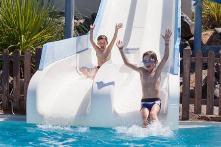 2 Kinder rutschen im Außenpool des Ferienparks Roompot Le Littoral eine Doppelrutsche hinunter