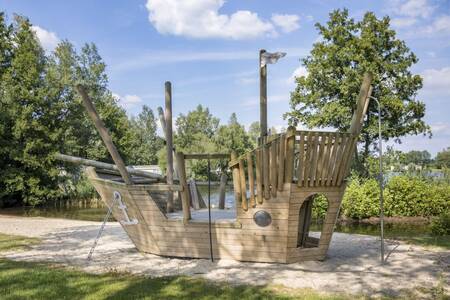 Ein hölzernes Spielschiff auf einem Spielplatz im Ferienpark Roompot Recreatiepark de Tolplas