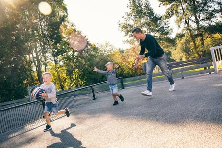 Vater spielt Fußball mit 2 Kindern auf einem Fußballfeld im Roompot Vakantiepark Weerterbergen