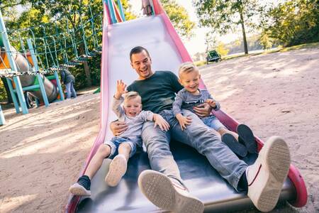 Vater mit 2 Kindern auf einer Rutsche auf einem Spielplatz im Roompot Vakantiepark Weerterbergen