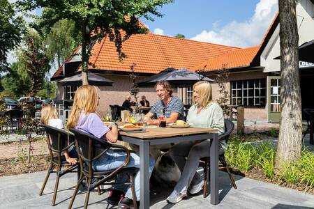 Familie isst auf der Terrasse des Restaurants des Ferienparks Topparken Resort Veluwe