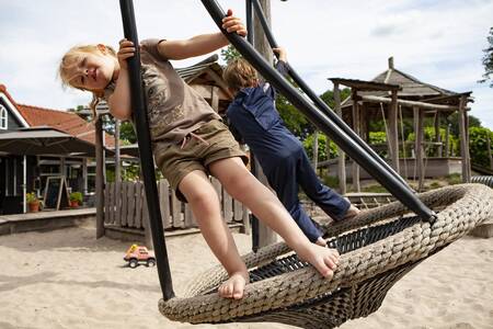 Kinder auf einer Schaukel auf einem Spielplatz im Ferienpark Sandberghe